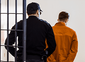 Officer escorting a person in an orange jumpsuit into custody, reflecting the criminal defense work of Simmrin Law Group