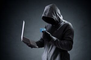 Hooded figure holding a credit card and laptop illustrating identity theft cases handled by Simmrin Law Group